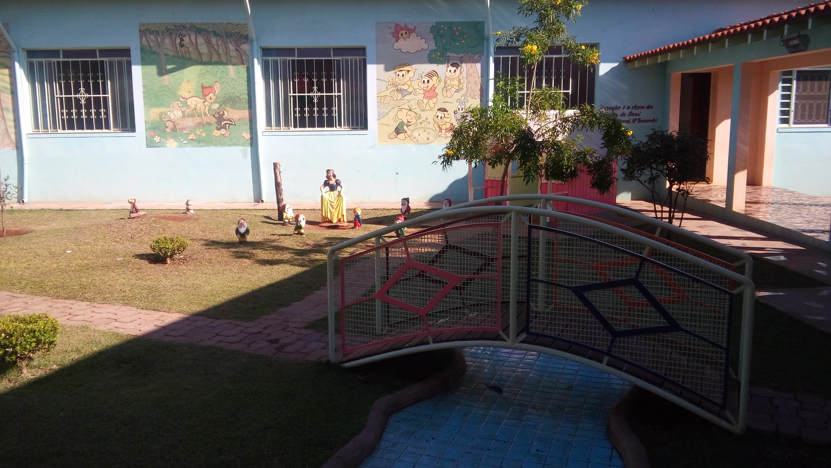 Área externa da Casa da Criança de Cândido Mota, com jardim, ponte decorativa e murais infantis na fachada